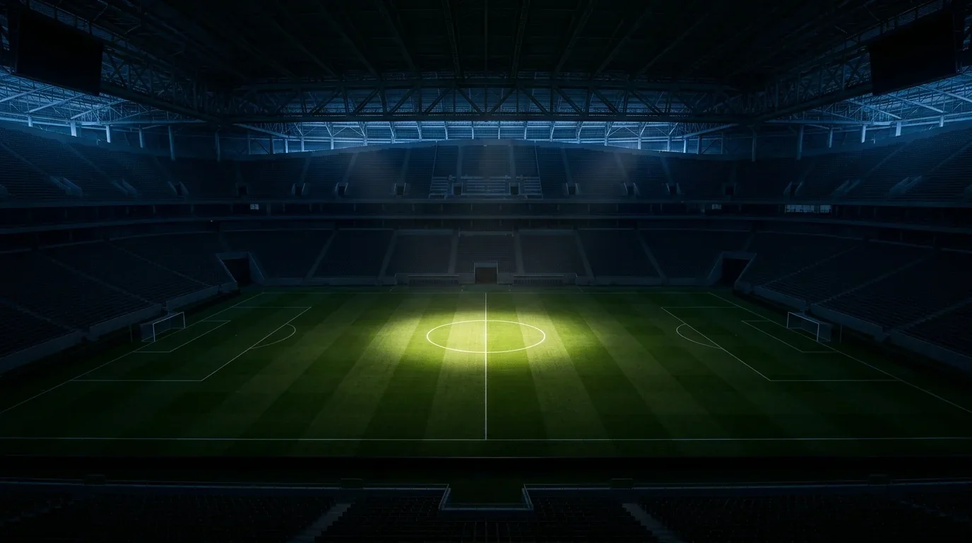 Pojedynczy reflektor oświetla środek murawy na wielkim stadionie z zamkniętym dachem, reszta trybun w półmroku, atmosfera meczu o wielką stawkę
